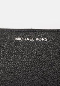 Svart texturerad läderplånbok med präglad logotyp "MICHAEL KORS" i silver. Slät yta med detaljer i pebblat mönster.