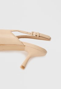 Sandalia de tacón de cuero beige con puntera abierta y diseño recortado. Cuenta con una delgada correa en el tobillo y un tacón de aguja esbelto. Acabado mate.