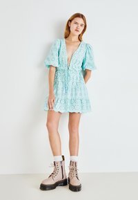 Robe bleu clair en broderie anglaise avec de courtes manches bouffantes, taille cintrée et jupe à volants. Associée à des bottes beiges à lacets et des chaussettes blanches.