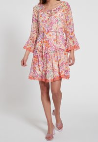Květinové šaty s dlouhými zvonovými rukávy. Vyrobené z lehké látky v pastelových odstínech růžové, oranžové a fialové. Rukávy s volánkovým lemem a zavazovací výstřih.