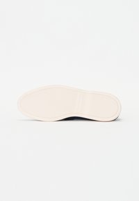 Witte zool sneaker met een gestructureerd donker bovenmateriaal. Kenmerkt zich door een ronde neus en een gladde rand, zonder zichtbare branding of accenten.