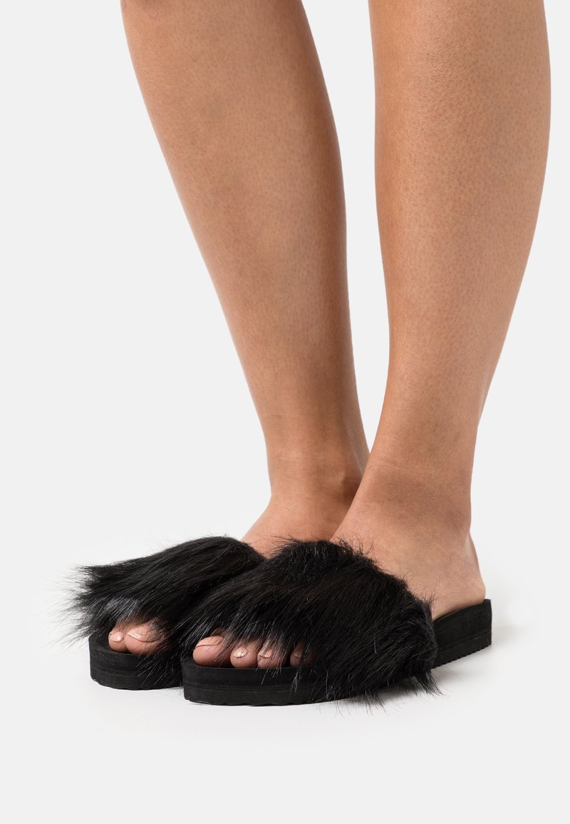 Black fur slide sandals with a wide, fluffy upper and a textured rubber sole, showcasing an open-toe design.