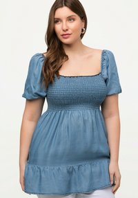 Denimblaues Oberteil mit einem gerafften Oberteil, kurzen Puffärmeln und einem Rüschensaum. Leichter Stoff mit weicher Textur.