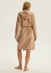 Kapturowa szlafrok w miękkim beżowym materiale, z długimi rękawami, wiązanym paskiem i długością do połowy łydki. Gładka faktura o luksusowym wyglądzie.