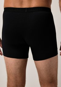 Boxers en coton noir avec une texture lisse et une taille élastique portant le nom de la marque en relief. Coupe ajustée, longueur mi-cuisses.