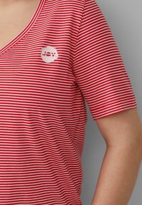 Rood-witte gestreepte T-shirt met een V-hals, korte mouwen en een cirkelvormig wit logo met de tekst "JOY" op de bovenste linkerzijde.