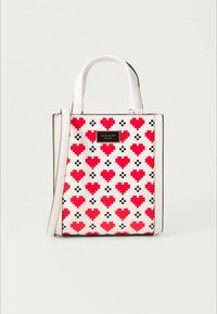 Bílá kabelka s červenými pixelovanými srdíčky a černými detaily. Má dvě rukojeti a odnímatelný ramenní popruh. Zlatá kovová plaketa s logem na přední straně.