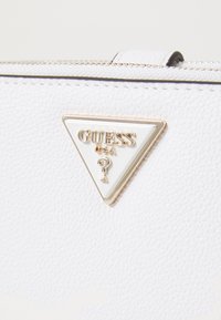 Valge tekstureeritud sünteetilisest nahast käekott, millel on kolmnurkne kuldne ja valge logo silt. Omab kuldseid sisusid ja tõmblukkude detaile.