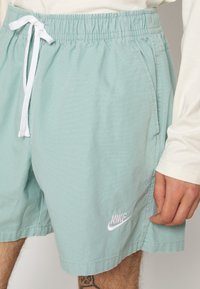 Ljust blå idrottsshorts i vävt tyg. Har en elastisk midja med dragsko och en vit broderad Nike-logotyp på sidan.