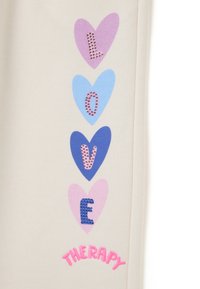 Beige stof met een verticale rangschikking van harten in roze, blauw en paars. Tekst spelt "LOVE" met juweelversieringen en "THERAPY" in het roze.