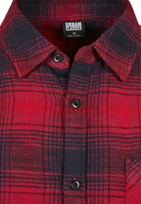 Chemise à carreaux rouge et noir avec un col boutonné, des boutons noirs, et un tissu à texture douce. L'étiquette indique "URBAN CLASSICS" et la taille "M".
