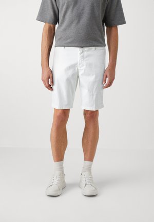 Pantalones cortos de algodón blancos con corte recto, que cuentan con bolsillos frontales y cierre con botón. Combinados con una camiseta gris de manga corta y zapatillas blancas.
