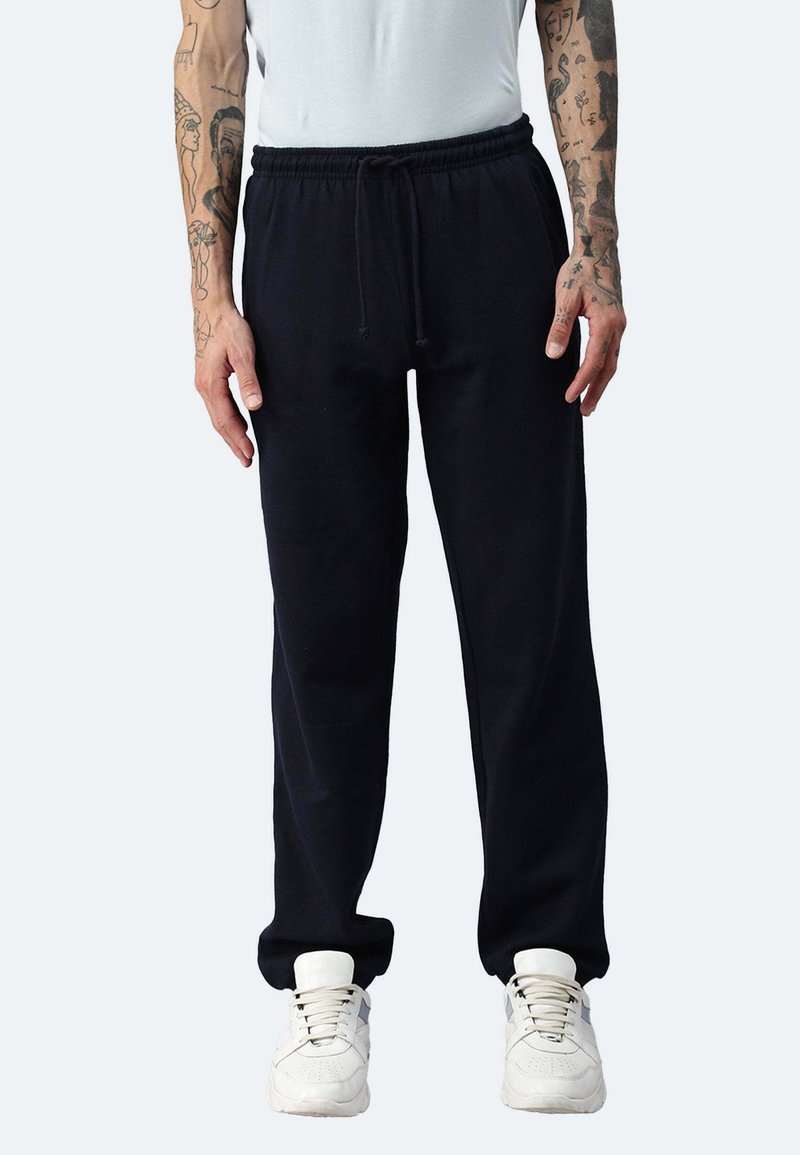 Schwarze Fleece-Jogginghosen mit elastischem Bund und Kordelzug, ausgestattet mit Seitentaschen und schmal zulaufenden Bündchen, kombiniert mit weißen Sneakers.