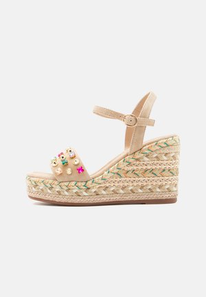 Sandalia cuña beige con correa en el tobillo, suela plataforma trenzada de yute y adornos de gemas coloridas en la correa delantera.