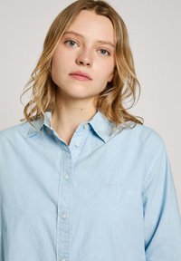Camicia azzurra chiaro con colletto, realizzata in tessuto morbido. Presenta un piccolo logo sul petto ed è caratterizzata da una vestibilità rilassata.