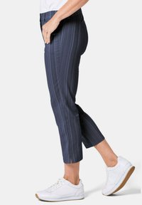 Marineblauwe cropped broek met verticale strepen, voorzien van een rekbare tailleband en zijsplitten aan de zoom, gecombineerd met witte sneakers.