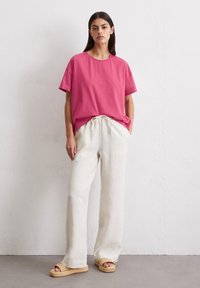 Roze katoenen t-shirt met korte mouwen, gecombineerd met losse witte linnen broeken en geweven sandalen met een gestructureerde strap.