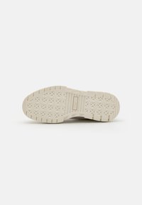 Semelle de sneaker en caoutchouc blanc cassé avec une surface texturée et un motif en étoile pour l'adhérence. Présente des bords crantés et une zone de marque centrale.
