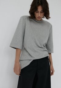 Szary, oversize t-shirt z krótkimi rękawami, okrągłym dekoltem i luźnym krojem, połączony z ciemnymi, szerokimi spodniami. Miękka tekstura.