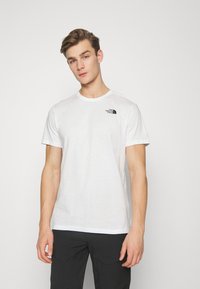 T-shirt bianco in cotone con scollatura a girocollo, maniche corte e un piccolo logo nero sul petto sinistro. Vestibilità standard, texture liscia.