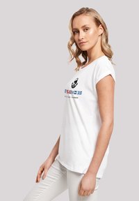 White cotton t-shirt with rolled sleeves, featuring a black graphic and colored text. Straight cut design with side slits for ease of movement.