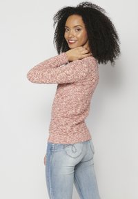 Rožinė megzta palaidinė su tekstūruotu raštu, prigludusios formos, apvalia iškirpte, ilgomis rankovėmis; derinama su šviesiai mėlynomis džinsomis su dekoratyviais siūlais.