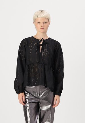 Blusa nera trasparente con un sottile motivo a foglia, scollatura rotonda e chiusura con nastro; presenta maniche lunghe e vita arricciata. Indossata con pantaloni metallici lucidi.