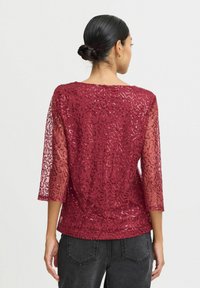 Bordo proziran top s 3/4 rukavima, ukrašen teksturiranim uzorkom i suptilnim šljokicama. Lagani materijal doprinosi eleganciji.
