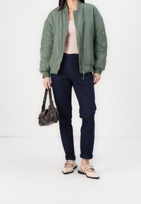 Zielona kurtka bomberka, jasnoróżowy top, granatowe spodnie, beżowe baleriny ze paskami oraz brązowa torebka. Gładkie tekstury i swobodny design.