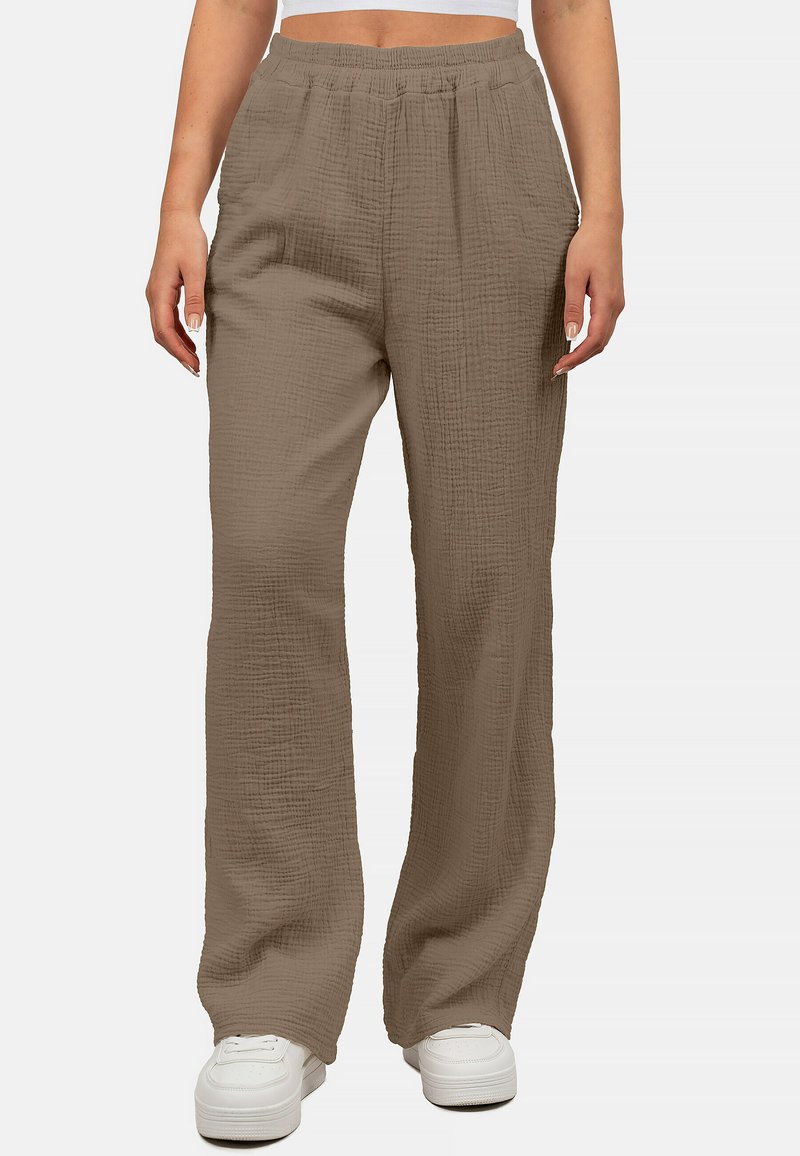 Weite Hose aus einem weichen, strukturierten taupefarbenen Stoff; mit einem elastischen Bund und seitlichen Taschen, kombiniert mit weißen Sneakern.