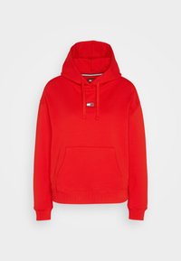 Sweat à capuche rouge à manches longues avec poche avant, cordons et petit logo Tommy Jeans blanc et bleu sur la poitrine, sur fond blanc.