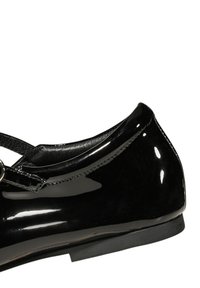 Scarpa in pelle verniciata nera con punta arrotondata, finitura lucida e una sottile fascia decorata con una fibbia argentata. Suola piana in gomma.