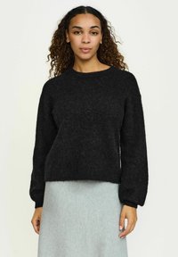 Must mustras, mille ümmarguse kaeluse ja pikad, kergelt puffitatud varrukatega. Pehme, tekstuurne kangas ja lühike lõige.