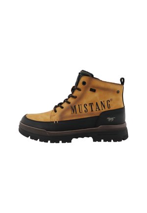 Tan- en zwarte hoge Mustang-merklaars met dikke rubberen zool en zwarte veters, zijaanzicht op witte achtergrond.