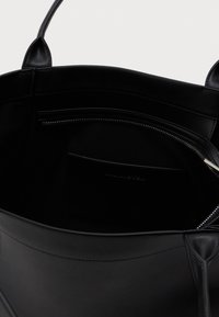 Schwarze Leder-Tasche mit Griffen, teilweise geöffnet und zeigt eine Reißverschlusstasche im Inneren und einen glatten Innenstoff.