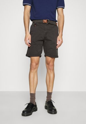 Pantalones cortos de algodón gris oscuro con puños enrollados, con un cinturón tejido marrón, combinados con zapatos negros y calcetines marrones. Camiseta polo azul marino de manga corta.