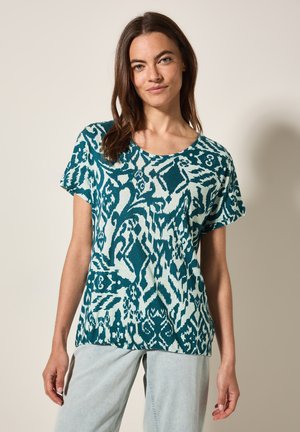 Top in maglina a maniche corte di colore teal con scollo rotondo. Presenta motivi astratti in tonalità più chiare e un tessuto testurizzato.