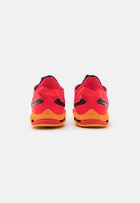 Red athletic shoes with a mesh upper, black accents, and a yellow sole. Features a padded collar and distinctive heel design.