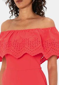 Abito rosso senza spalline con sovrapposizione in pizzo ricamato e arricciato. Tessuto liscio, cuciture visibili e ritagli decorativi sul pizzo.