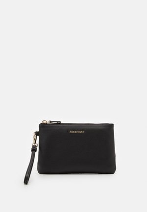 Mała kopertówka na nadgarstek z czarnej skóry, z złotym zamkiem błyskawicznym i logo "Coccinelle", wyposażona w odpinany pasek na nadgarstek, przedstawiona na białym tle.