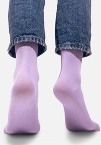 Liliowe skarpetki bawełniane pokazane na nagich stopach, w połączeniu z podwiniętymi dżinsami. Skarpetki mają gładką fakturę i dopasowany krój.