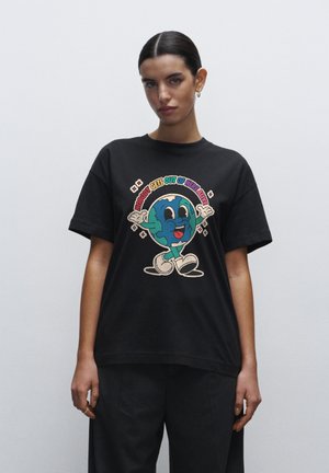 Sort bomulds T-shirt med et farverigt cartoon design af jorden med et smilende ansigt, arme og teksten "NOBODY GETS OUT OF HERE ALIVE."