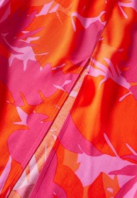 Tissu rose vif et orange avec des motifs abstraits de feuilles et des coutures visibles sur une surface textile lisse.