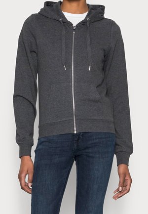 Grijze zip-up hoodie van zachte stof, met een capuchon, trekkoord en voorkruiken. Gecombineerd met donkerblauwe jeans.