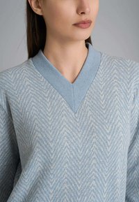 Maglione azzurro chiaro con scollo a V e motivo a spina di pesce. Tessuto morbido con un colletto a contrasto. Vestibilità rilassata.