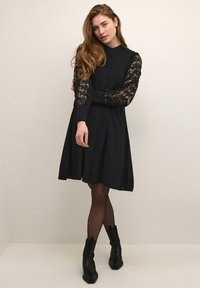 Black dress with lace long sleeves, button front, collar, and a flared skirt. Worn with black ankle boots and sheer tights.
