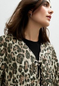 Quiltad jacka med leopardmönster i dämpade toner av grön, brun och beige, med knytning och en lätt, slät textur.