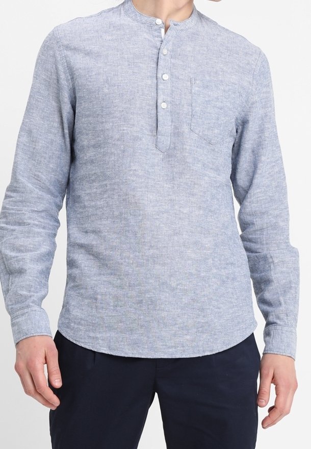 Homme portant une chemise en lin bleu clair à manches longues avec une patte boutonnée et une poche poitrine, associée à un pantalon bleu foncé.