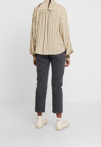 Camicia a righe beige e bianca con vestibilità ampia; abbinata a pantaloni grigi alla caviglia e sneakers beige alte.