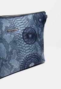 Niebieska teksturowana sakiewka z wzorem skóry węża, okrągłymi haftowanymi wzorami, złotym zamkiem błyskawicznym i małym złotym logo "Desigual".